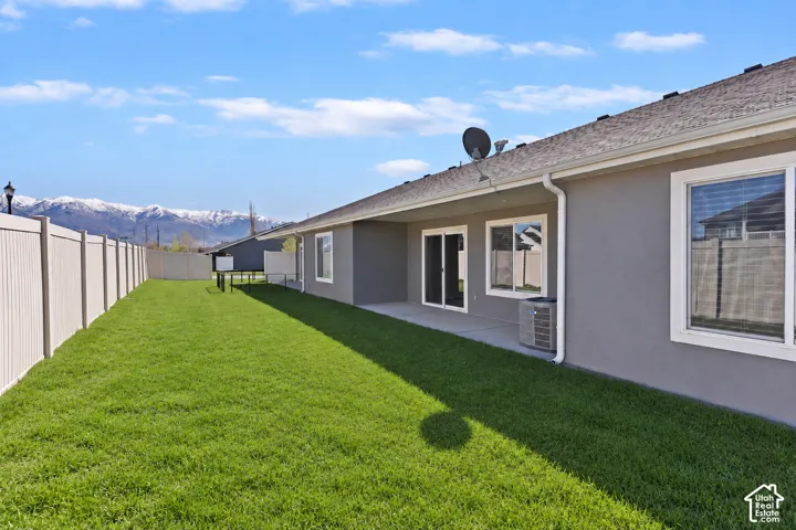 Expansive fenced backyard with a manicured lawn, concrete patio, and prominent mountain scenery