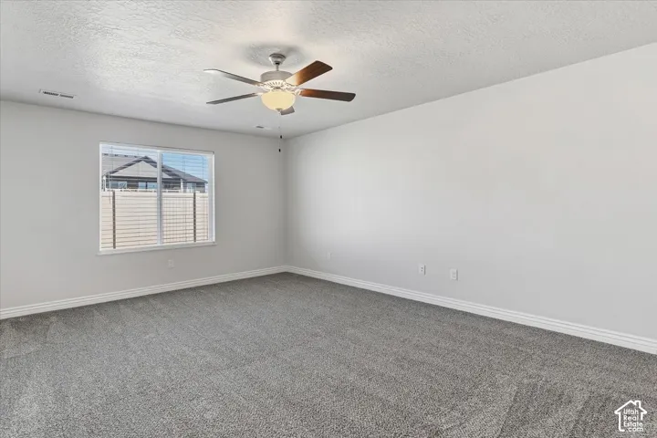 Spare room with dark carpet, a textured ceiling, and ceiling fan