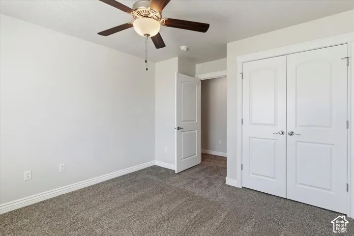 Unfurnished bedroom with dark colored carpet, a closet, a ceiling fan, and a textured ceiling