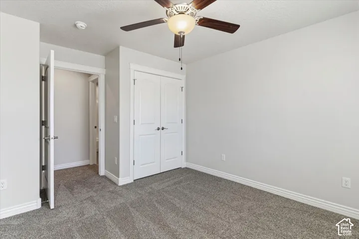 Unfurnished bedroom featuring a textured ceiling, dark colored carpet, a closet, and a ceiling fan