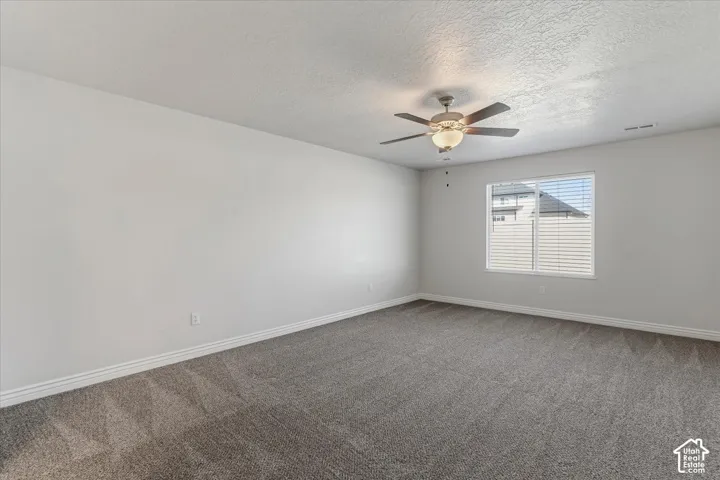 Unfurnished room featuring dark carpet, a ceiling fan, and a textured ceiling