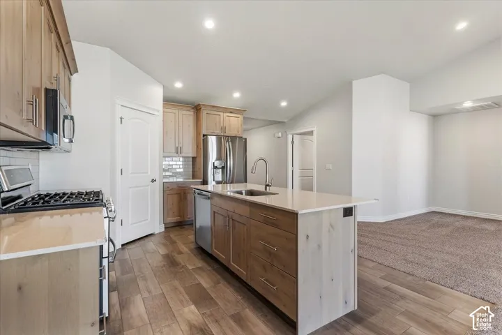 Kitchen featuring stainless steel appliances, tasteful backsplash, a center island with sink, wood tiled floors, and recessed lighting