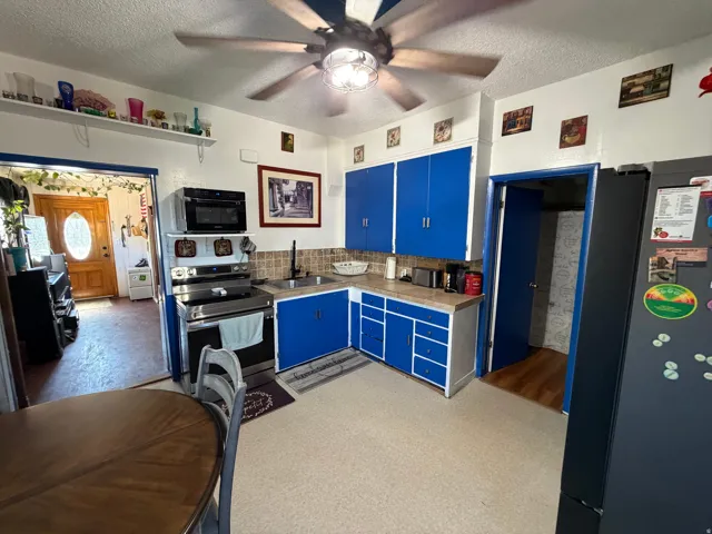 Kitchen featuring blue cabinetry, a textured ceiling, stainless steel appliances, ceiling fan, and tile counters