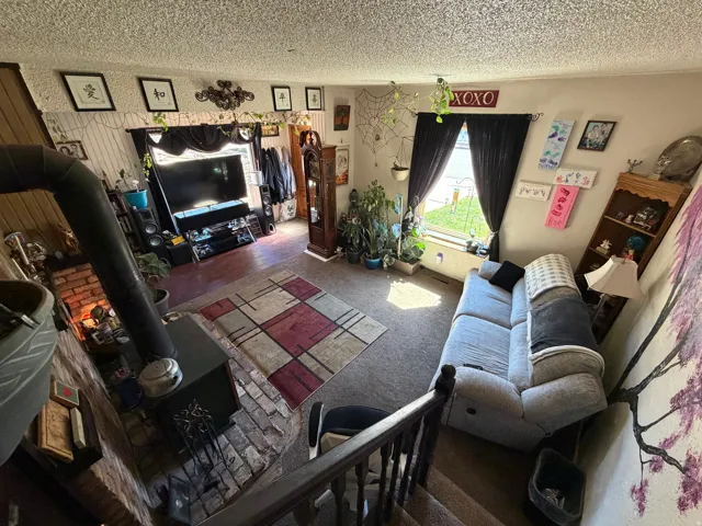 Living area featuring a wood stove, dark carpet, and a textured ceiling