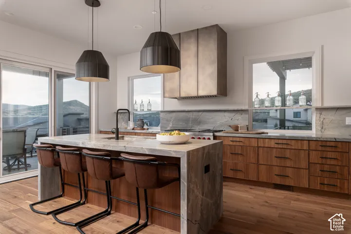 Kitchen featuring light stone counters, a kitchen breakfast bar, an island with sink, light wood-style flooring, and tasteful backsplash