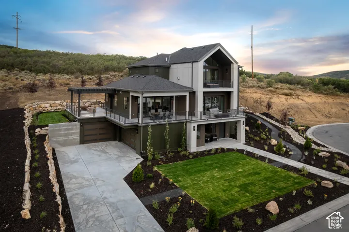 View of front of home with an attached garage, concrete driveway, a lawn, a balcony, and a patio area