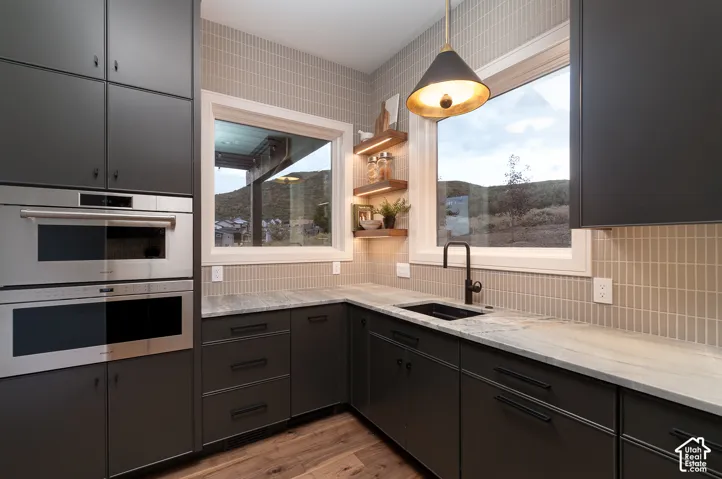 Dual tone kitchen featuring double oven, light stone countertops, hanging light fixtures, dark wood-type flooring, and dual tone cabinets