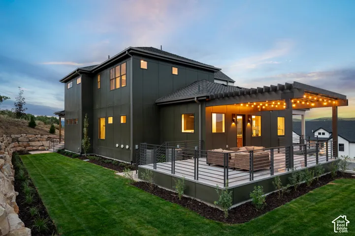 Back of house at dusk with a lawn, board and batten siding, a deck, and a pergola