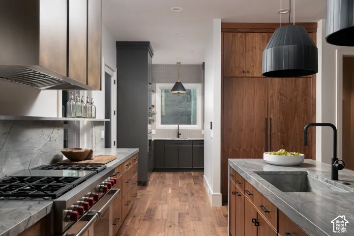 Dual tone kitchen with ventilation hood, stainless steel appliances, two tone cabinetry, dark stone countertops, and light wood-style flooring