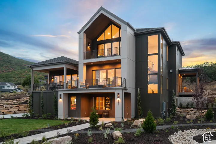 Back of property at dusk featuring a balcony, a lawn, a mountain view, and a patio area