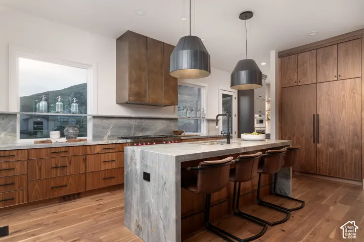 Kitchen featuring a breakfast bar area, light stone counters, decorative backsplash, a kitchen island with sink, and wood finish cabinets