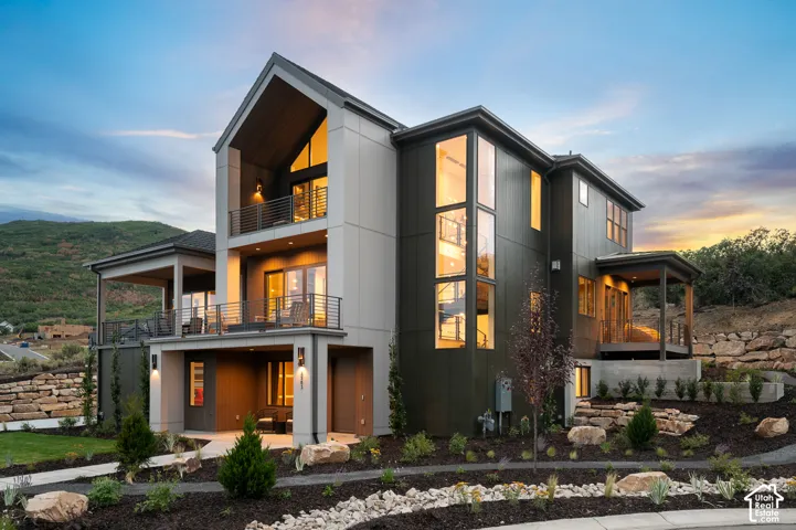 Back of property at dusk with a balcony and a patio area