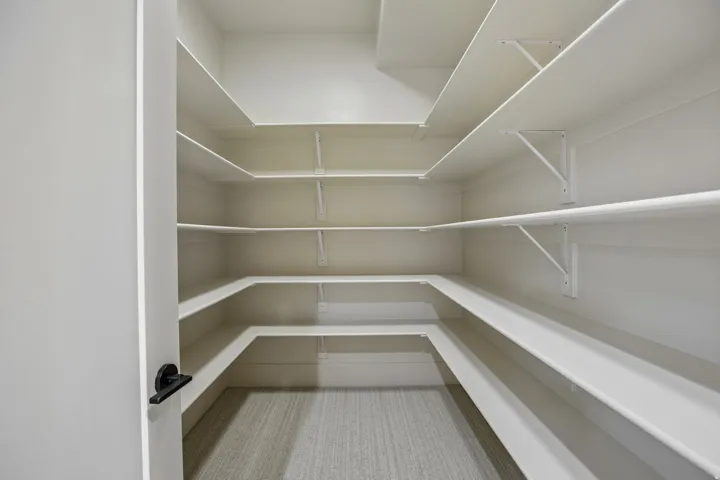 Walk-in pantry featuring extensive built-in shelving, durable white finishes, and light-toned flooring