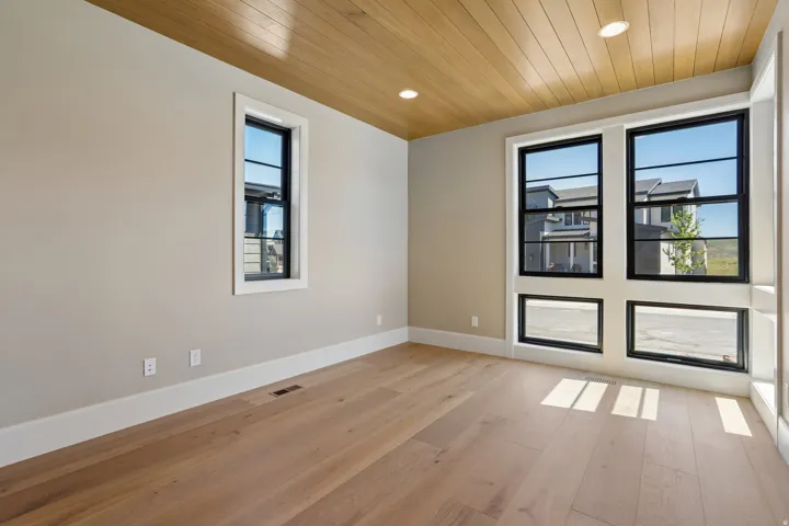 Spacious room featuring light wood-finish flooring, a wood-paneled ceiling, recessed lighting, and large windows with black frames