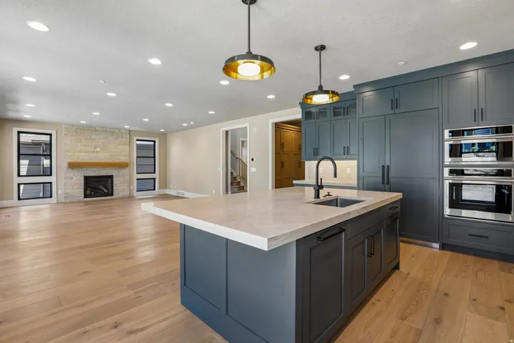 Gourmet kitchen featuring a large island with sink, integrated refrigerator, double wall ovens, extensive cabinetry, and wood-finish flooring