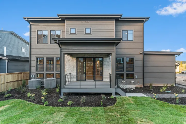 Modern exterior with multi-toned siding, covered patio with stone accent wall, and a manicured lawn
