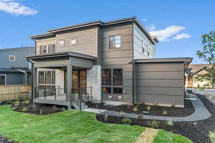 Modern exterior featuring horizontal siding, a covered deck with cable railing, stone accents, and a gravel walkway