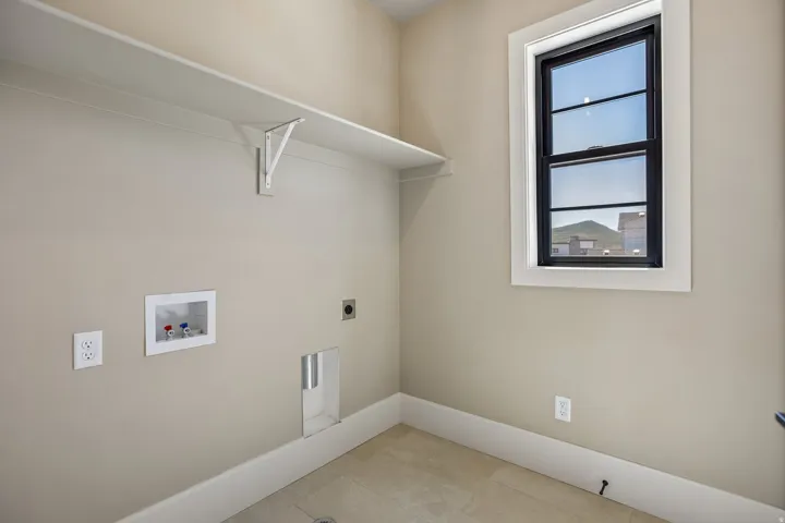 Utility room featuring a single window with black trim, tile flooring, wall-mounted shelving, and plumbing hookups