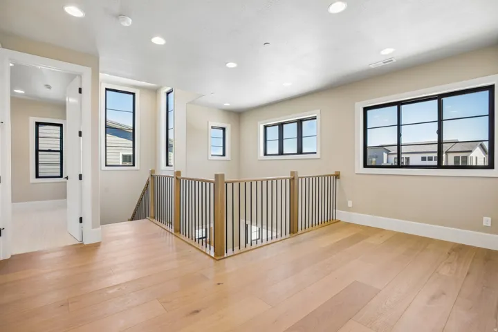 Hardwood flooring extends throughout this upper-level space featuring a contemporary wood and metal baluster railing, recessed lighting, and multiple black-framed windows