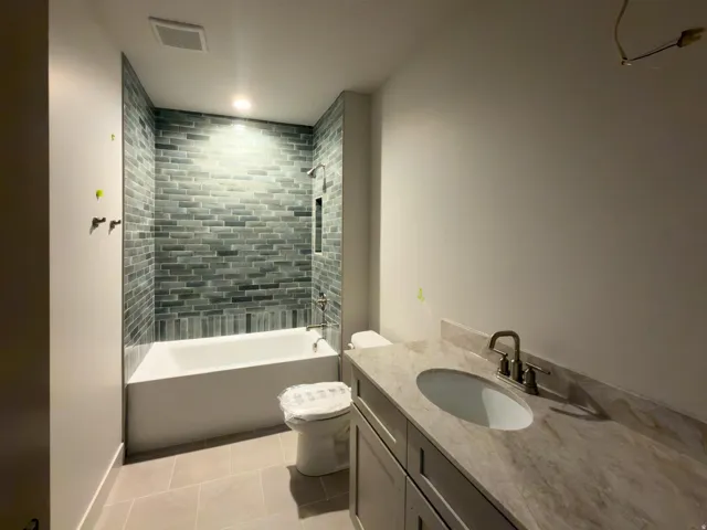 Sleek bathroom featuring a subway-tiled shower, white soaking tub, light-toned floor tiling, vanity with an integrated sink, and an elegant faucet