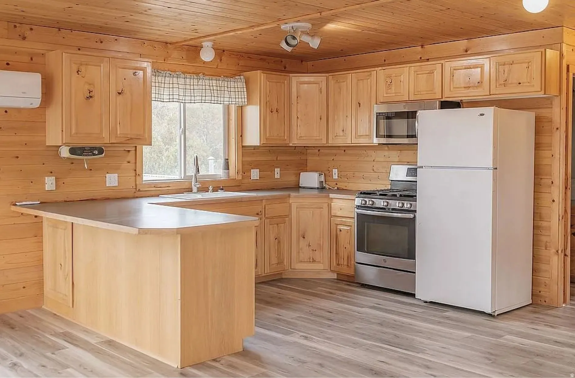 Kitchen with light wood finish cabinets, stainless steel appliances, light countertops, wood ceiling, and light wood-style floors