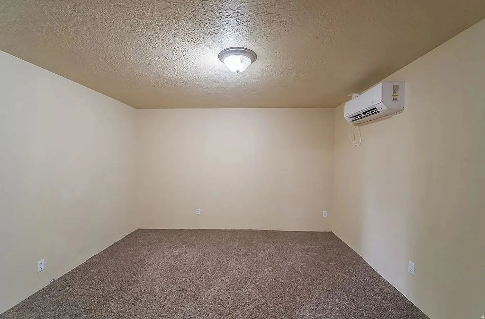 Carpeted empty room with a textured ceiling and a wall mounted mini split