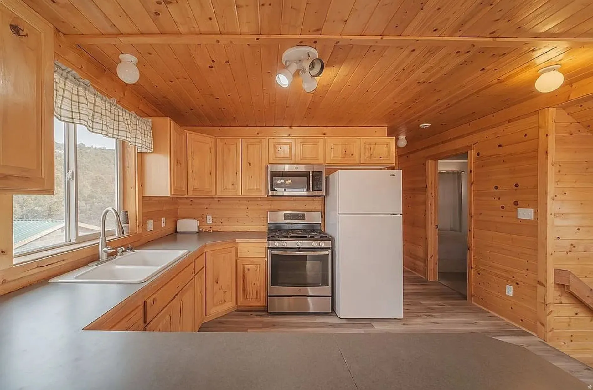 Kitchen with stainless steel appliances, light wood finish cabinets, light wood finished floors, light countertops, and wooden walls