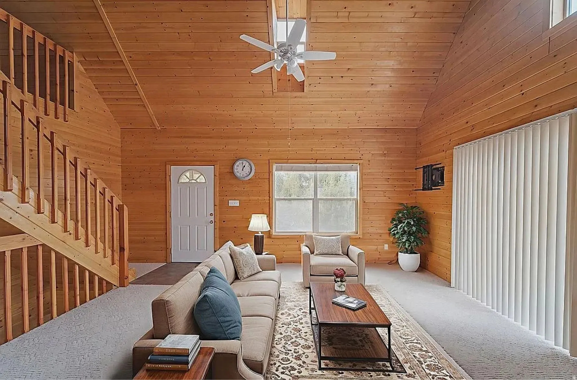 Carpeted living room featuring wooden walls, ceiling fan, and a vaulted wooden ceiling