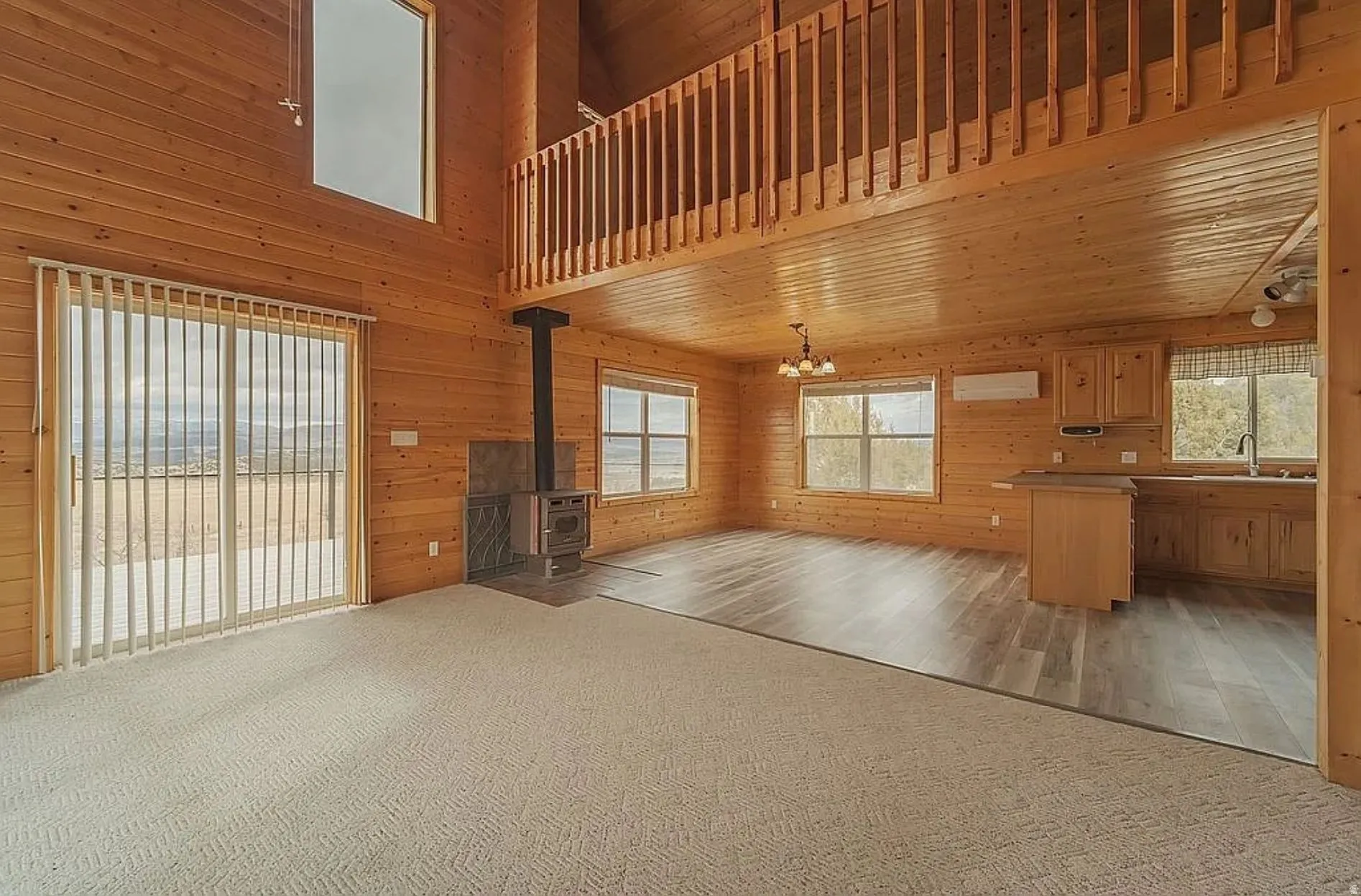 Unfurnished living room featuring wood walls, light carpet, a wood stove, a chandelier, and a high ceiling