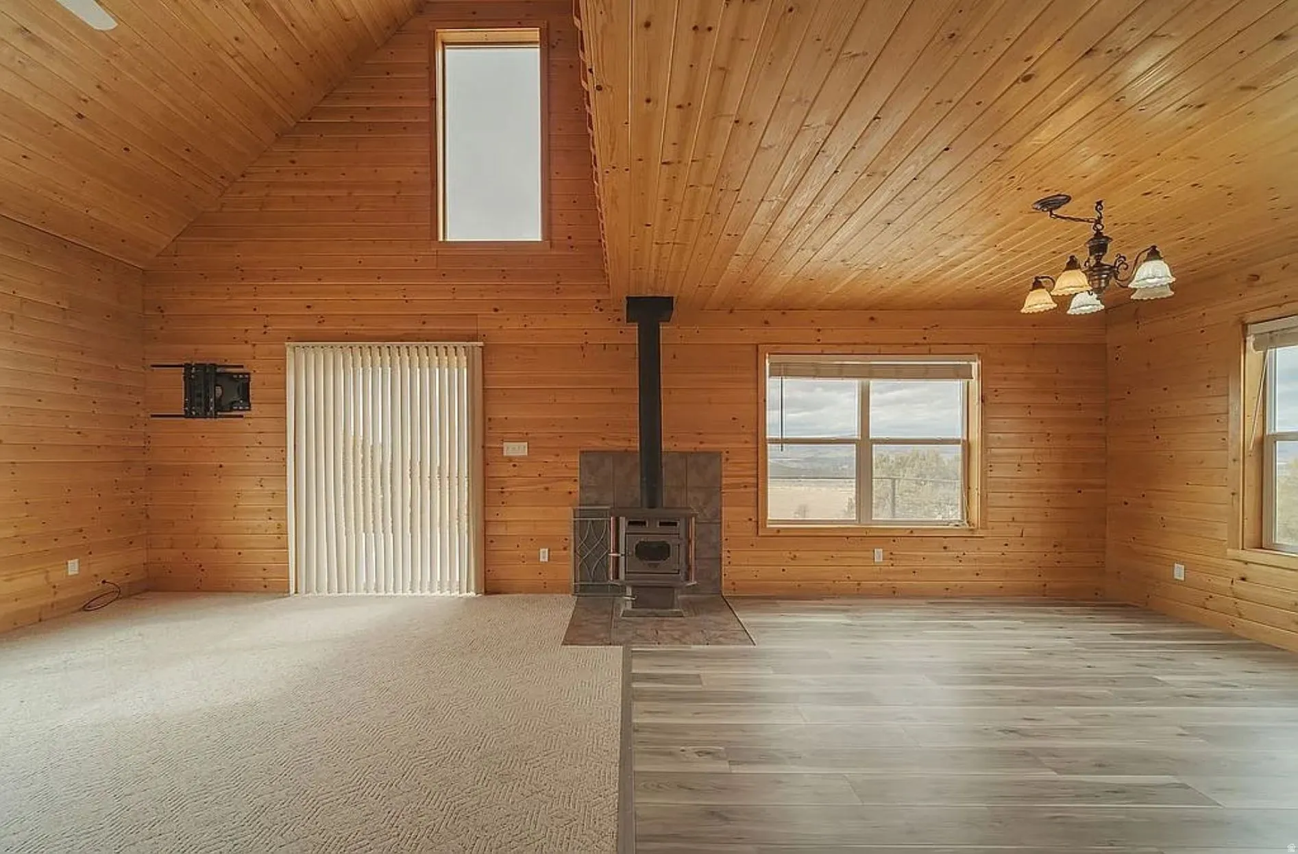 Unfurnished living room with a high wooden ceiling, wooden walls, a wood stove, suspended lighting, and wood finished floors