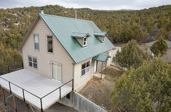 Rear view of property featuring a wooded view, a metal roof, and a wooden deck