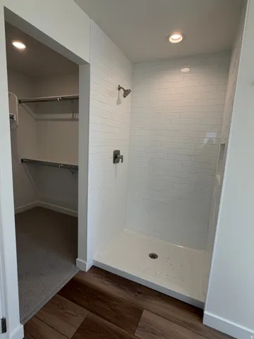 Full bath featuring recessed lighting, a spacious closet, dark wood finished floors, and a stall shower