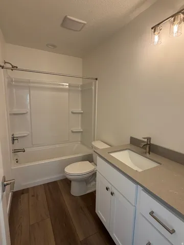 Full bathroom with vanity, dark wood-style flooring, shower / bath combination, and a textured ceiling
