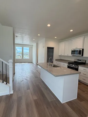 Kitchen with stainless steel appliances, white cabinets, dark wood-style flooring, an island with sink, and dark stone countertops