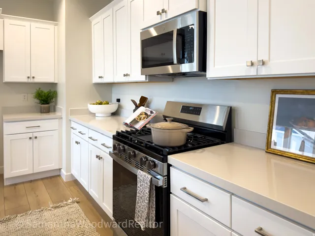 Kitchen featuring stainless steel appliances, white cabinets, light wood-style floors, and light stone counters