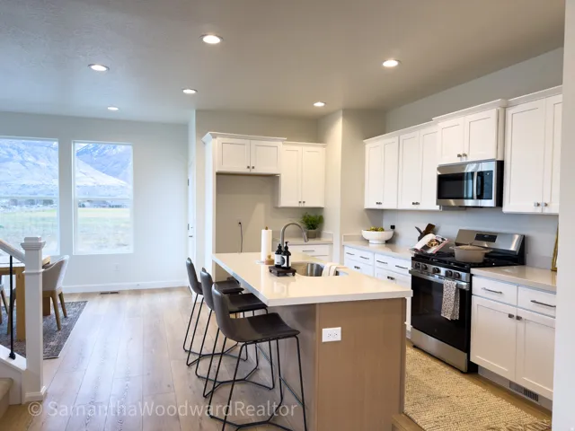 Two tone kitchen with stainless steel appliances, recessed lighting, a kitchen island with sink, a kitchen bar, and light wood finished floors