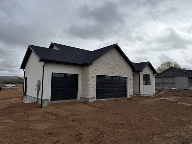 View of side of home featuring a garage, stone siding, a shingled roof, and dirt driveway