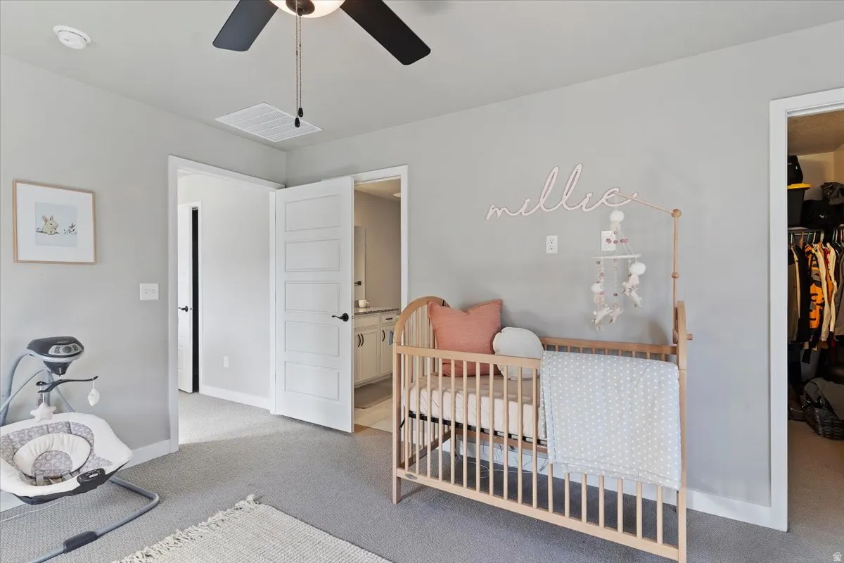 Bedroom with light colored carpet, a ceiling fan, and a spacious closet