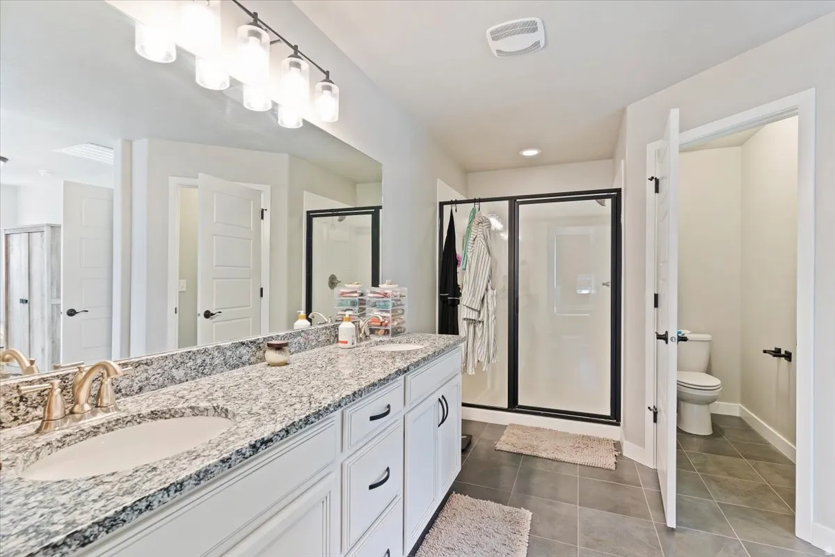 Full bathroom featuring a stall shower, double vanity, and dark tile patterned floors
