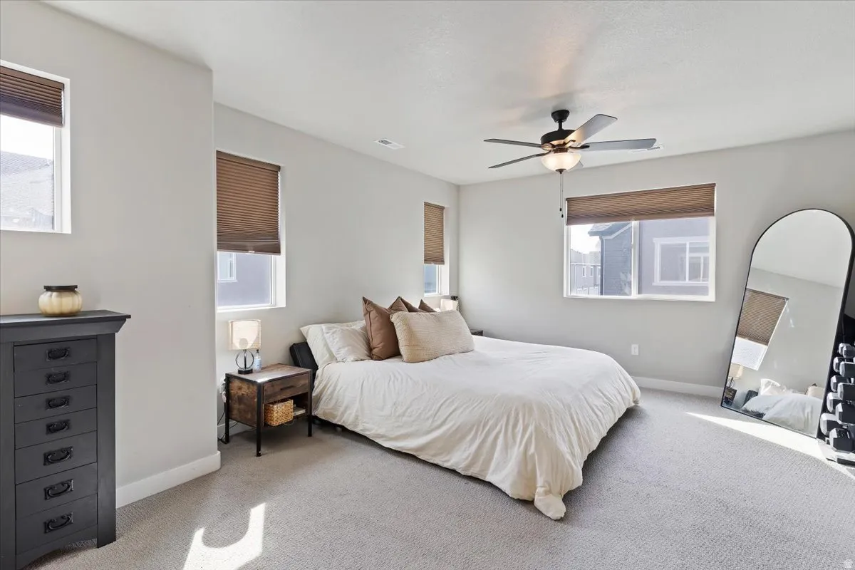 Carpeted bedroom featuring multiple windows and ceiling fan