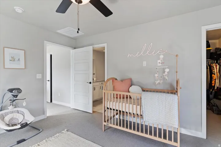 Bedroom with light colored carpet, a ceiling fan, and a spacious closet