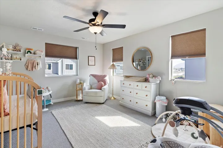 Bedroom with a nursery area, light colored carpet, multiple windows, and ceiling fan