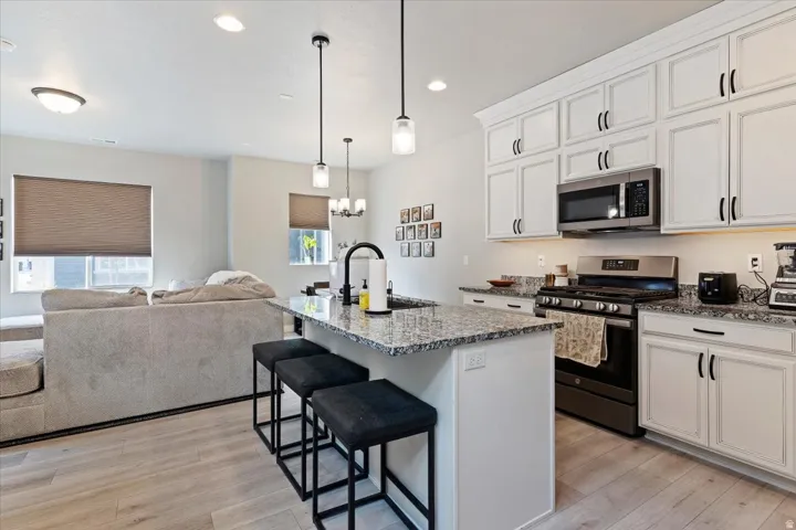 Kitchen featuring stainless steel appliances, a breakfast bar, light stone counters, a center island with sink, and light wood-style floors