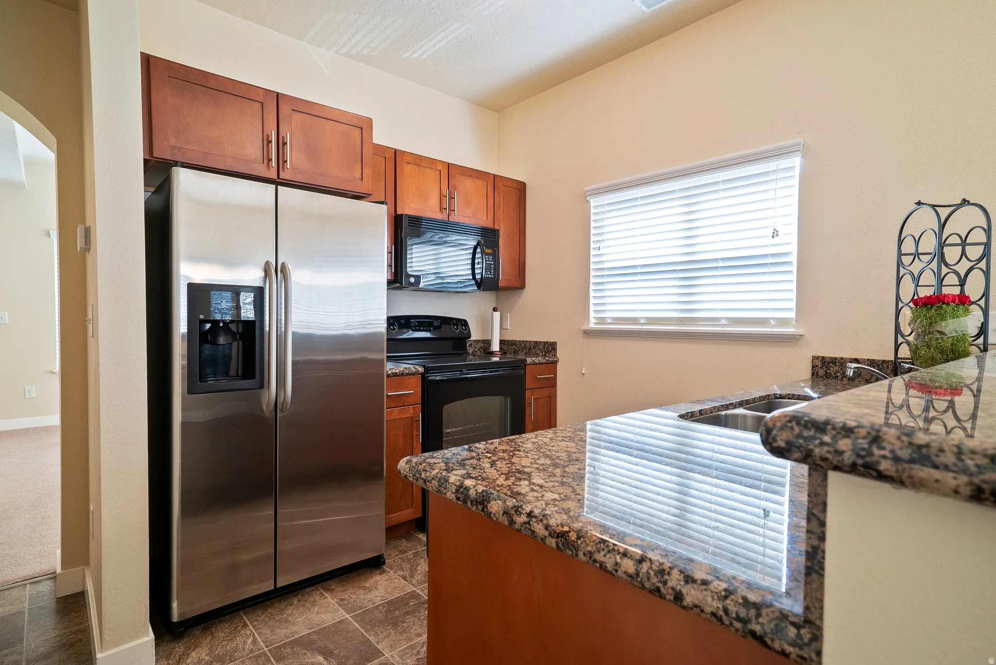 Kitchen with stainless steel refrigerator with ice dispenser, wood finish cabinetry, and granite countertops