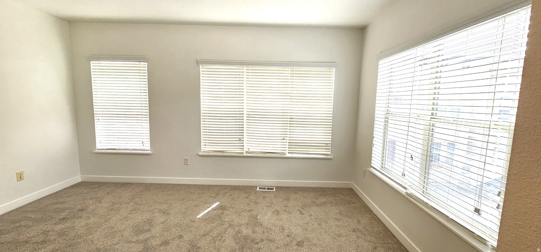 Carpeted room with multiple windows, white window blinds, and light-colored walls