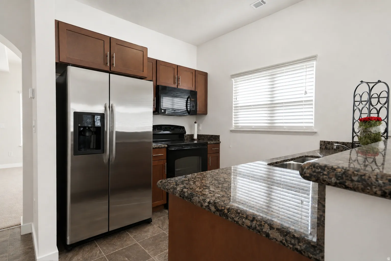 Kitchen featuring stainless steel appliances, dark wood-finish cabinetry, stone countertops, and tile flooring