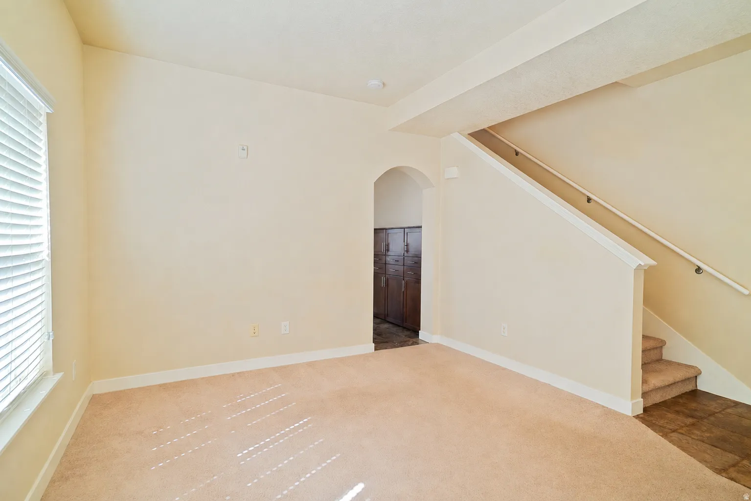 Carpeted living area with light-toned walls, white trim, and a window with blinds