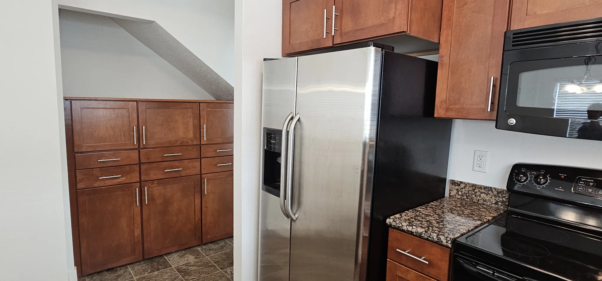 Stainless steel side-by-side refrigerator, extensive wood-finish cabinetry with brushed nickel hardware, built-in microwave, and stone-finish countertops