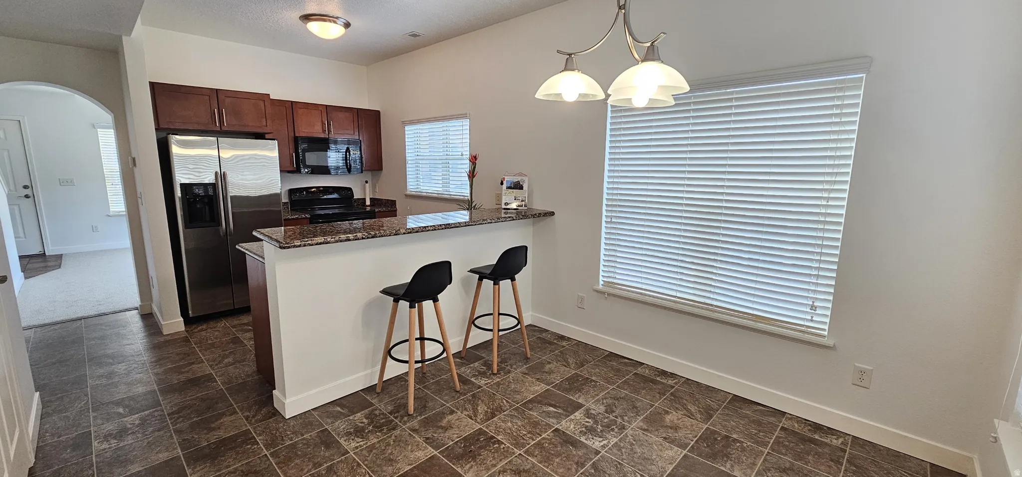 Kitchen with rich wood cabinetry, stainless steel appliances, a breakfast bar with stone-finish countertop, and tiled flooring