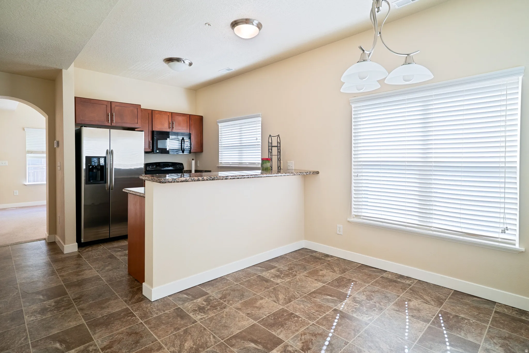 Kitchen featuring arched walkways, black appliances, pendant lighting, a peninsula, and granite countertops